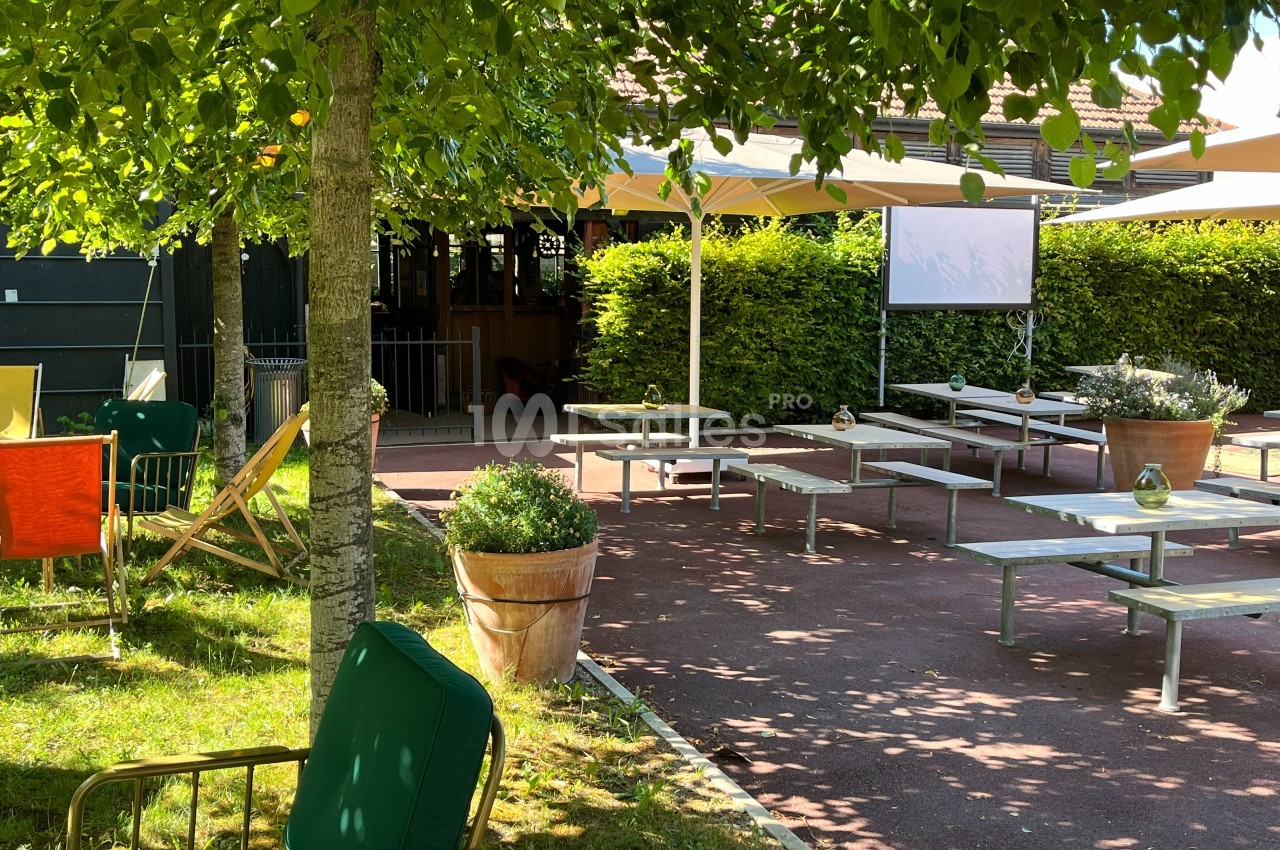 Terrasse ombragée avec tables, chaises et parasols, entourée de verdure et de plantes en pot.