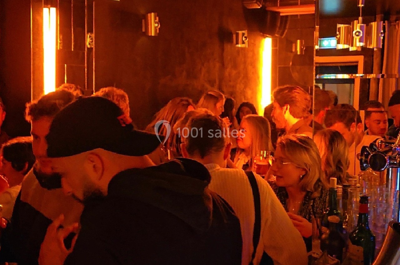 Groupe de personnes discutant et partageant un moment convivial dans un bar à l'éclairage tamisé et chaleureux.