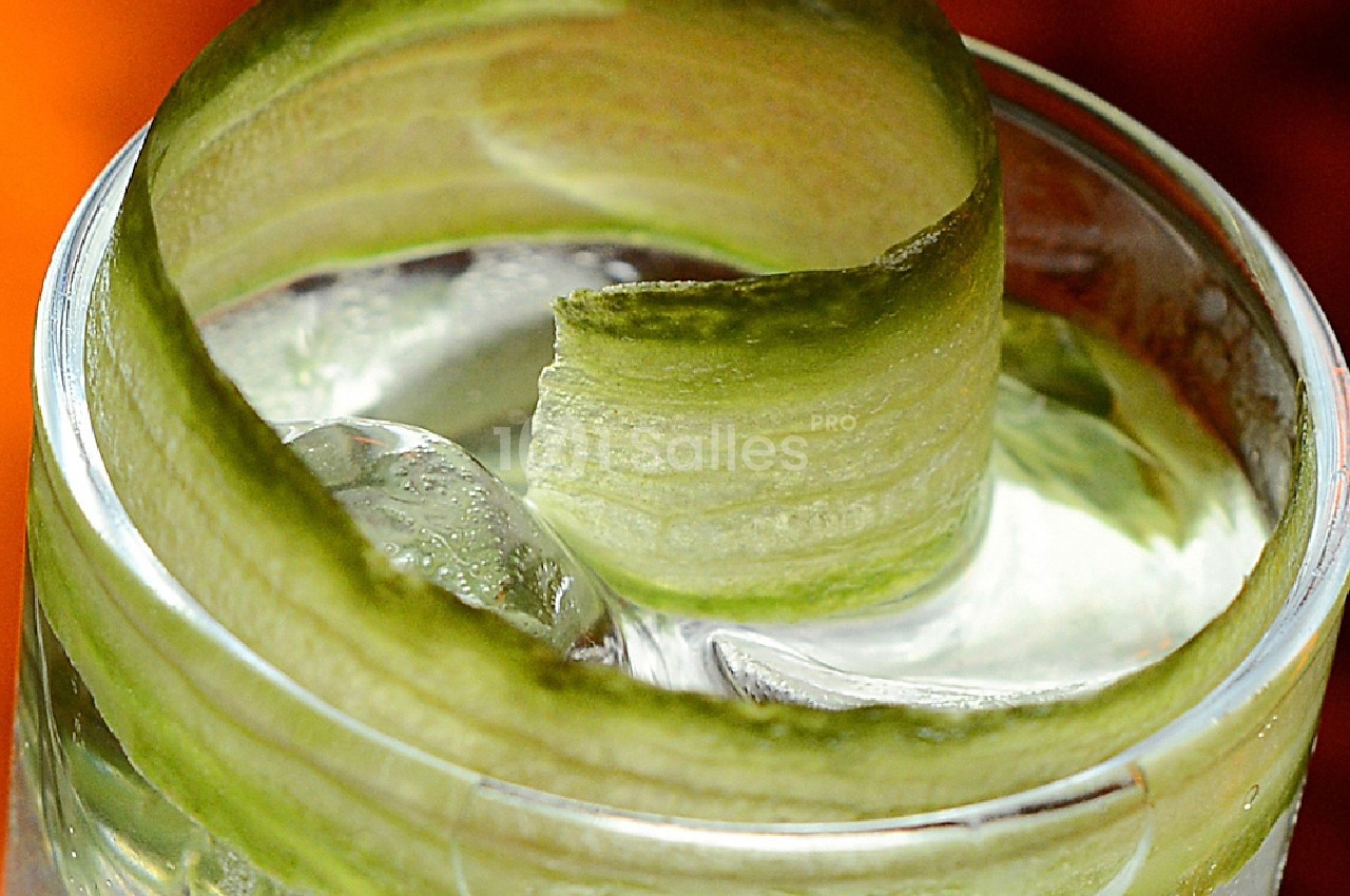 Verre de cocktail garni d'une spirale de concombre sur des glaçons.