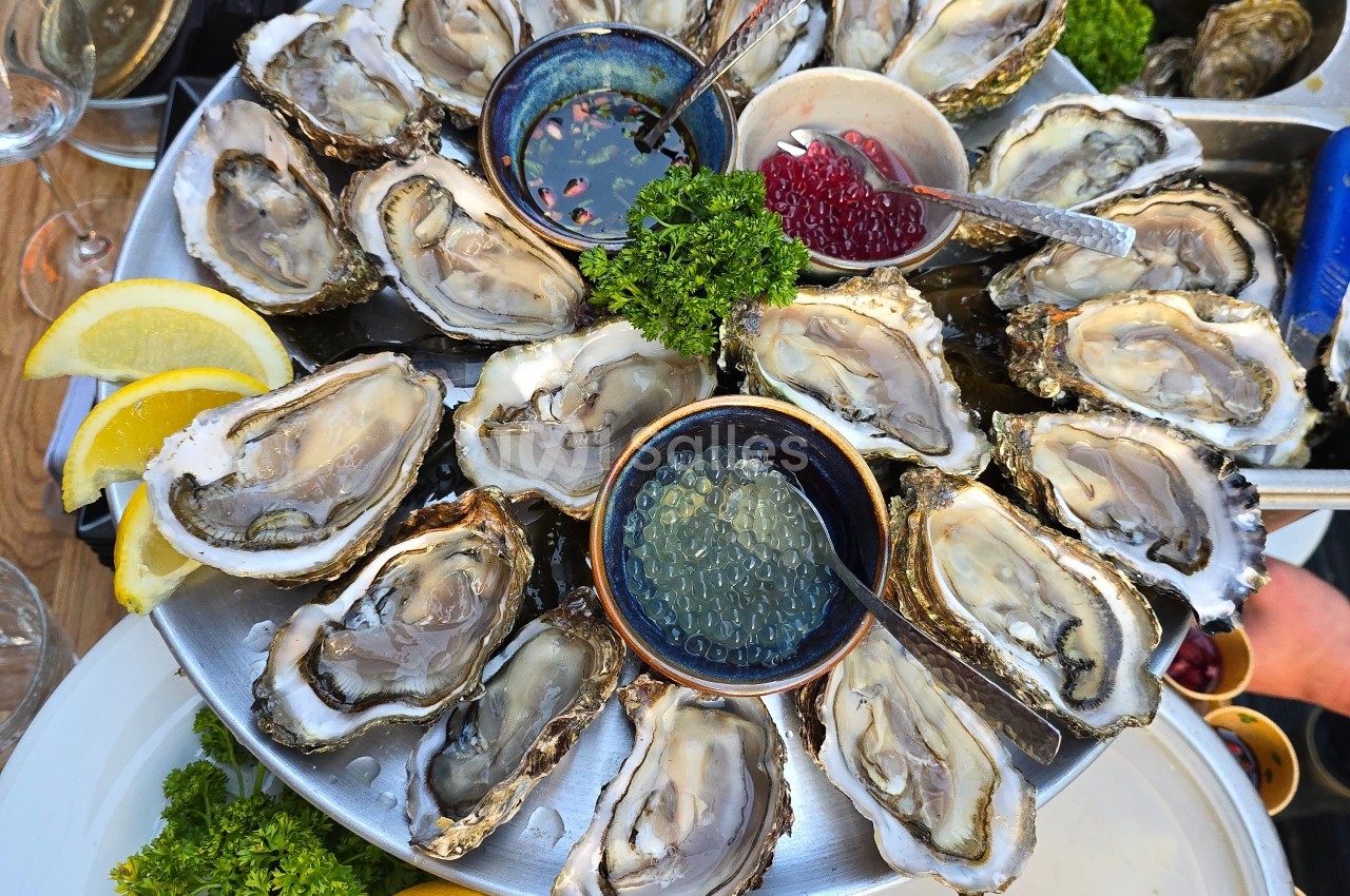 Plateau d'huîtres ouvertes servi avec citron, persil, et condiments dans des coupelles.