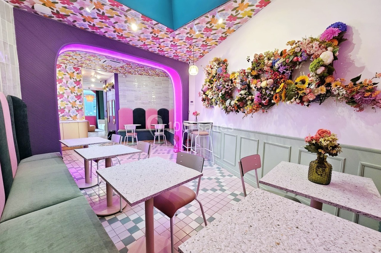 Salle de café colorée avec tables en marbre, chaises pastel et décoration florale murale vibrante.