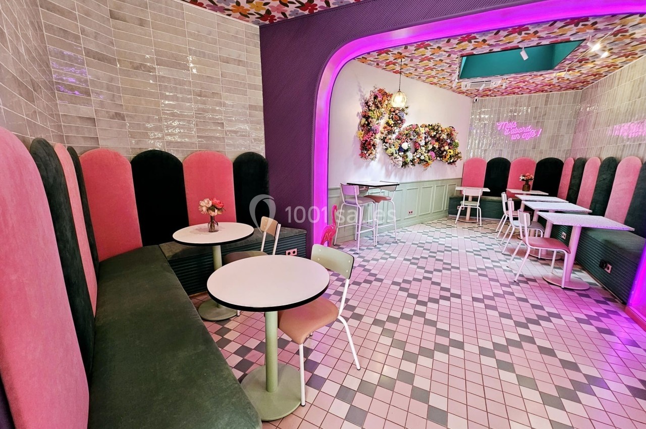 Salle de café colorée avec banquettes roses et vertes, tables rondes, murs fleuris et éclairage lumineux.