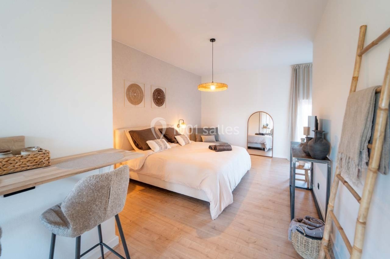 Chambre lumineuse avec lit double, décoration naturelle, mobilier en bois et miroir sur pied.