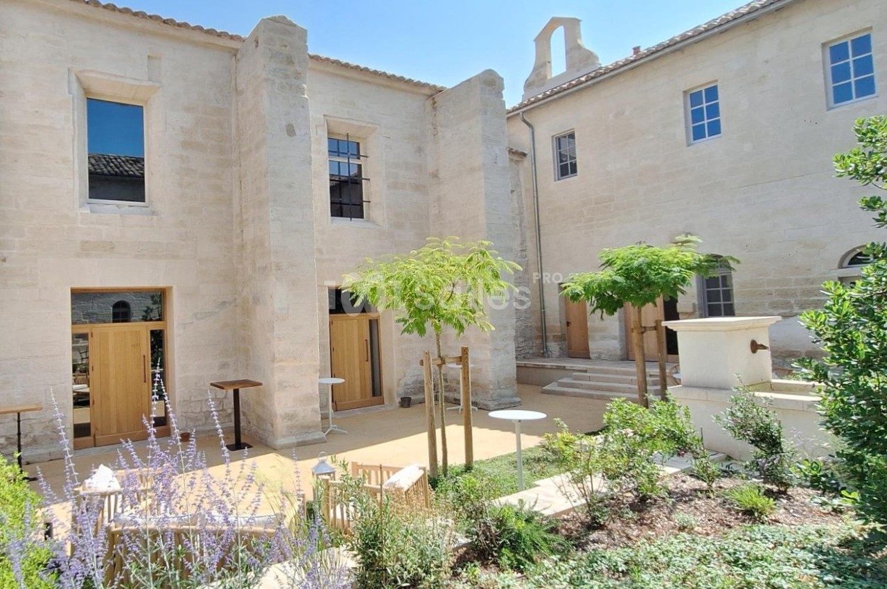 Cour intérieure d'un bâtiment en pierre claire avec végétation, tables et chaises disposées sur une terrasse.