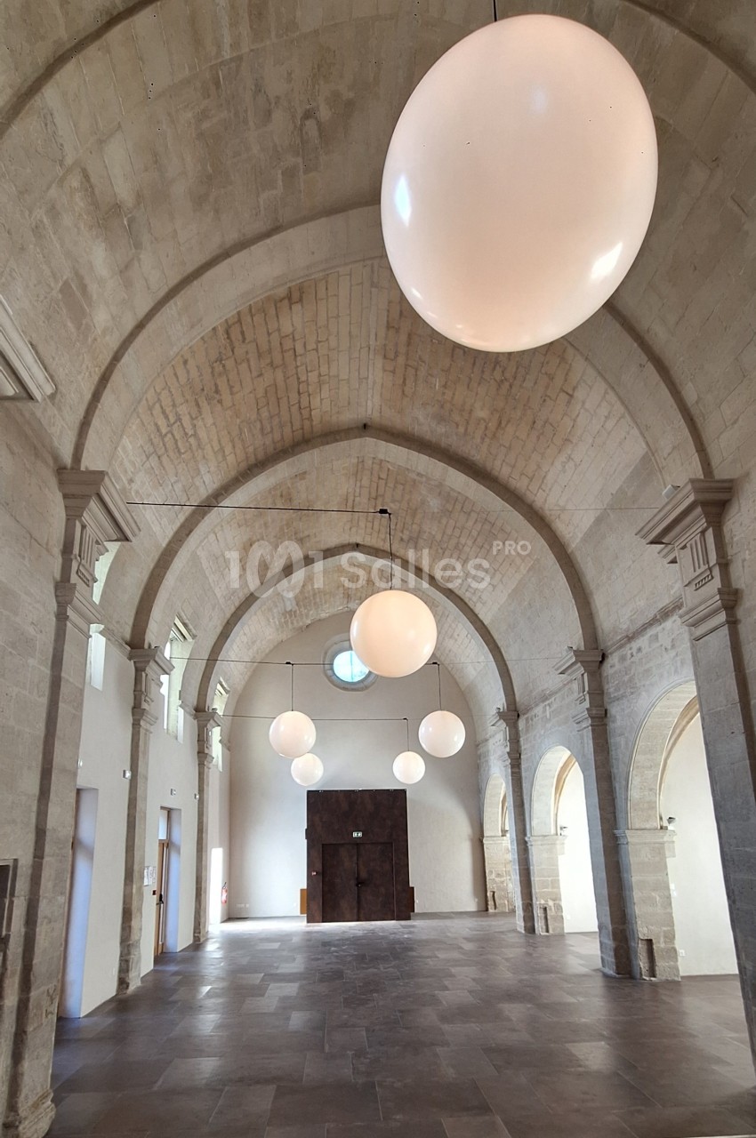 Salle voûtée en pierre avec éclairage suspendu sphérique et sol en dalles de pierre.