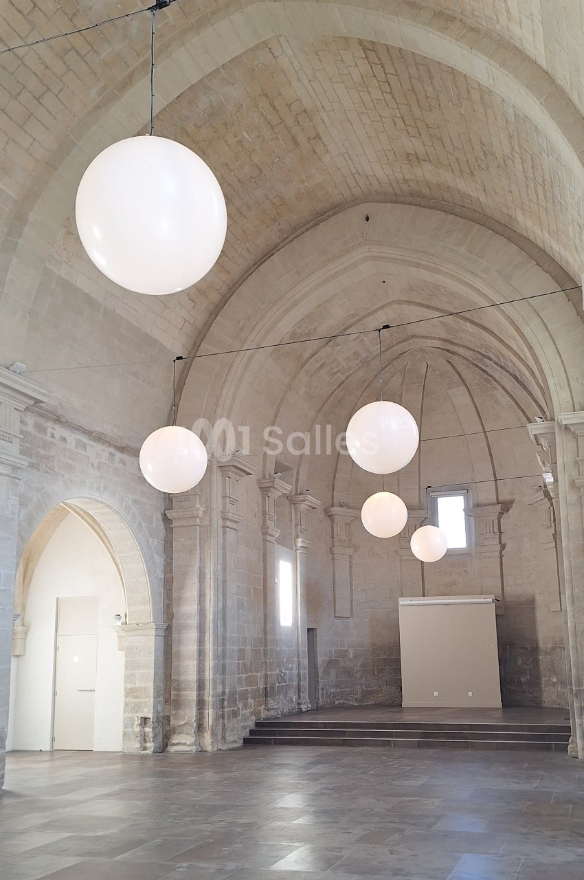 Salle voûtée en pierre avec des suspensions lumineuses rondes et un sol en dalles.