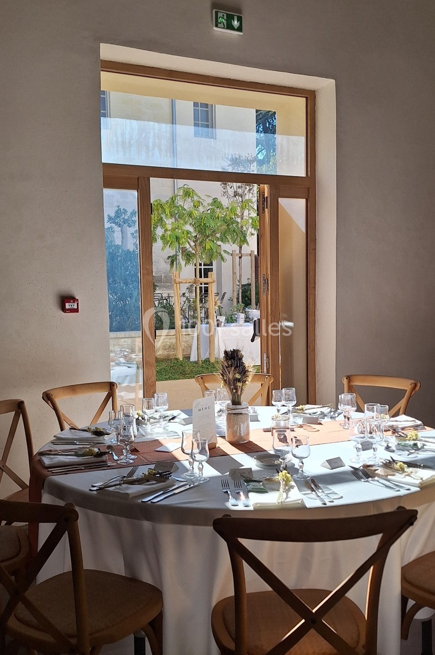 Table ronde dressée pour un repas, entourée de chaises en bois, près d'une porte vitrée donnant sur un jardin.