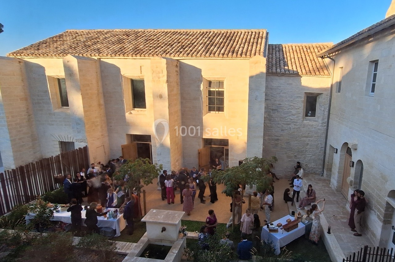 Groupe de personnes rassemblées dans une cour extérieure ensoleillée, entourée de bâtiments en pierre claire.