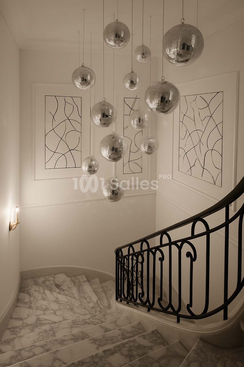 Escalier en marbre avec rampe en fer forgé, éclairé par des suspensions sphériques argentées et des appliques murales.