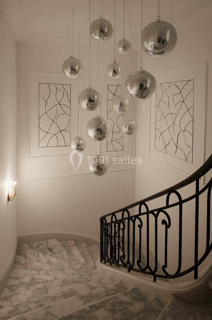 Escalier en marbre avec rampe en fer forgé, éclairé par des suspensions en forme de boules miroir.