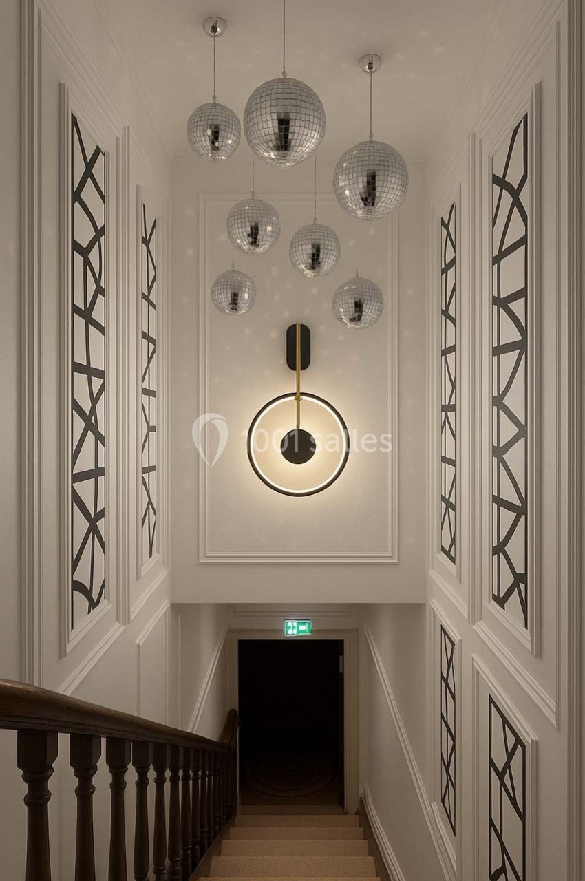 Escalier intérieur avec murs ornés de motifs géométriques, suspension lumineuse centrale et boules décoratives au plafond.