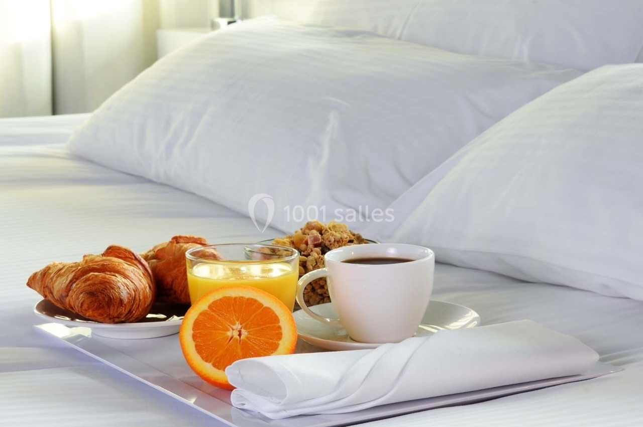 Petit-déjeuner avec croissants, jus d'orange, café et céréales servi sur un plateau sur un lit blanc.