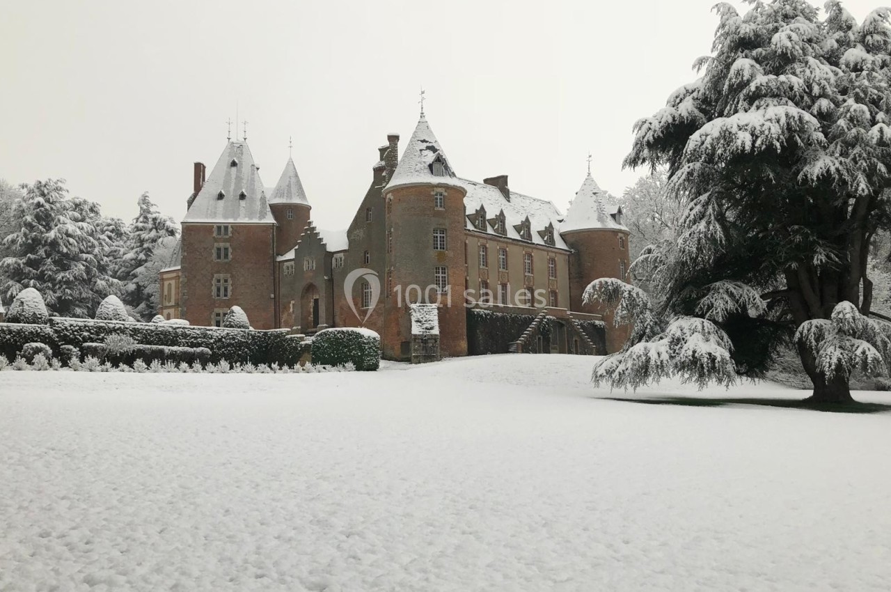 Château en pierre entouré d'arbres et d'un jardin recouvert de neige en hiver.