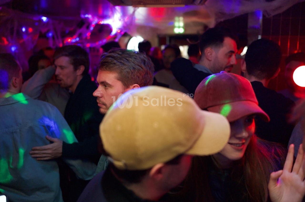 Groupe de personnes discutant et dansant dans un espace sombre décoré de lumières colorées et toiles d'araignée.
