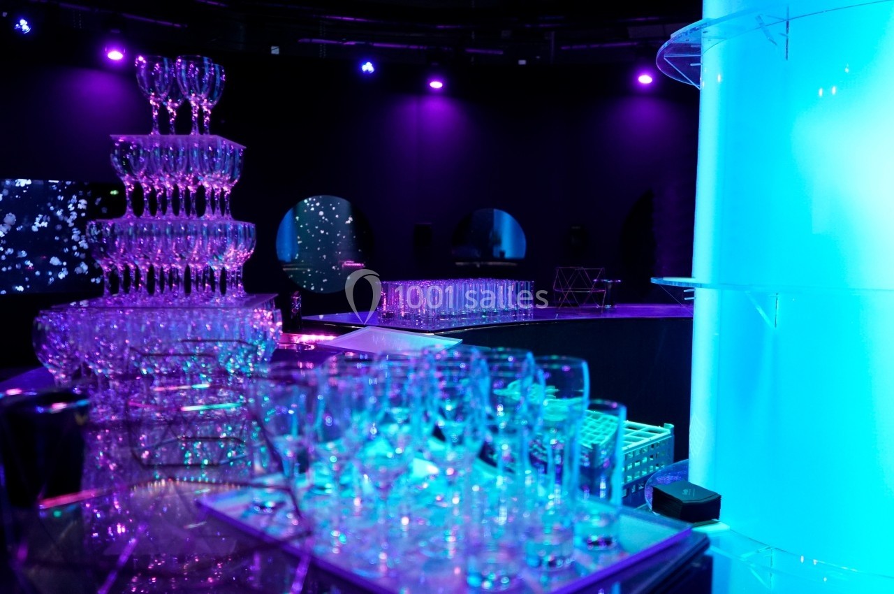 Tour de coupes en verre illuminée dans une ambiance tamisée avec éclairage violet et bleu.