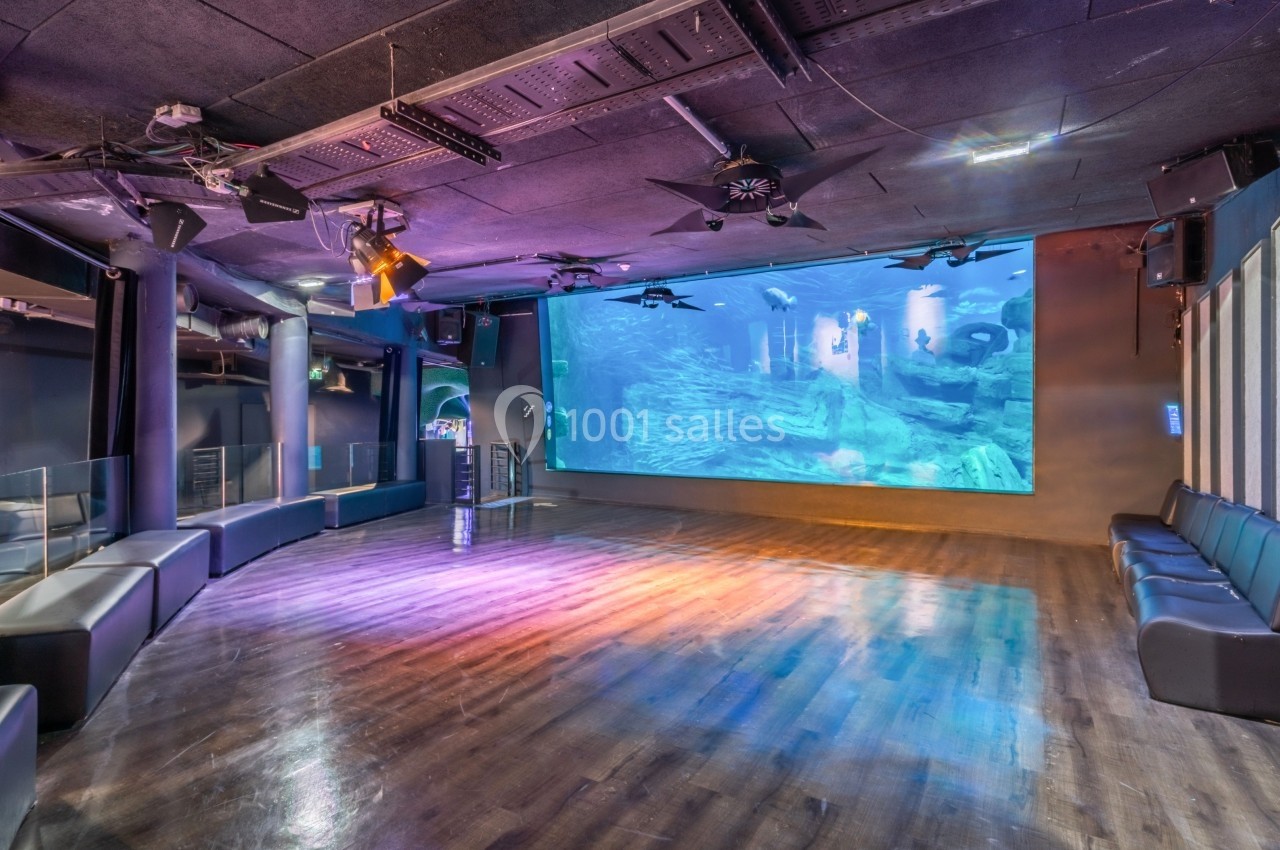 Salle vide avec parquet brillant, grands écrans muraux affichant une scène sous-marine et éclairage coloré.