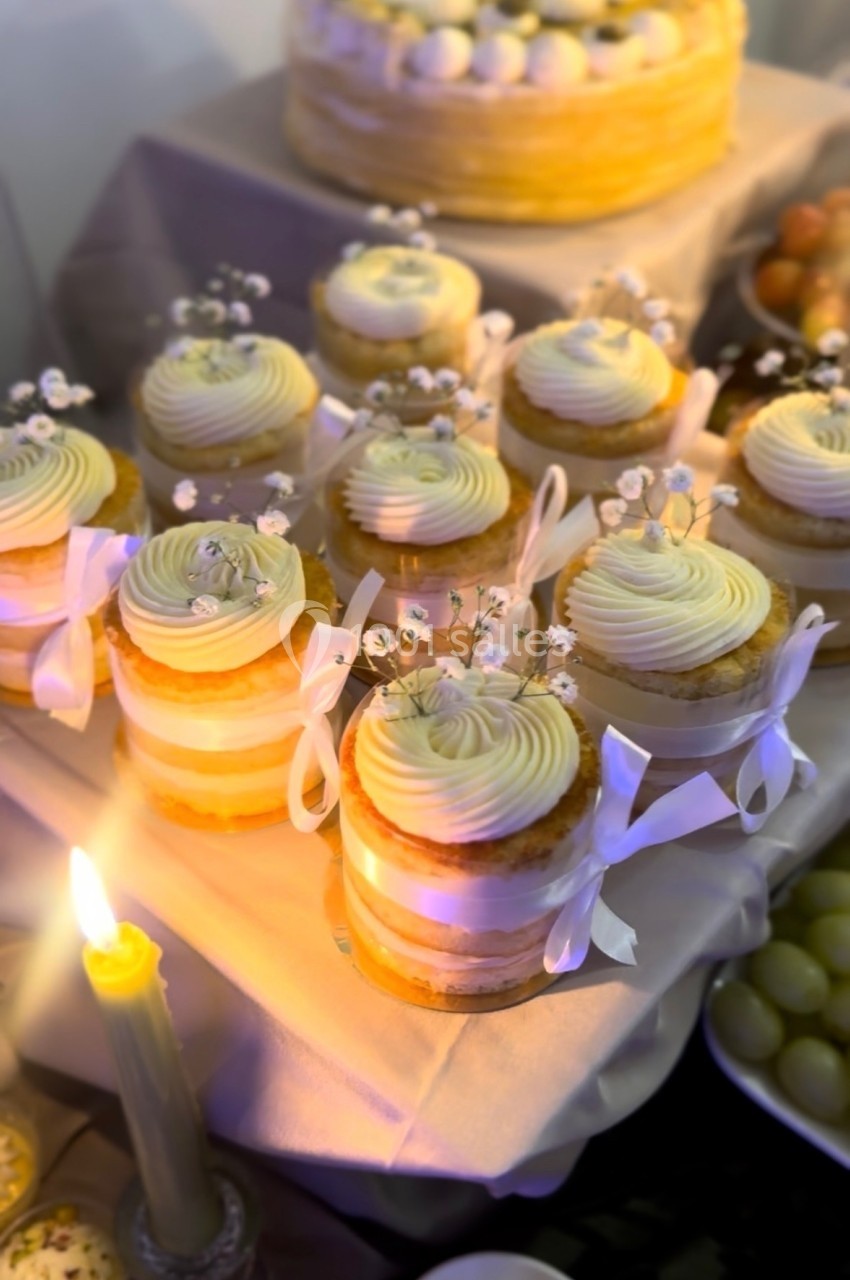 Petits gâteaux individuels décorés de fleurs blanches et rubans, disposés sur une table éclairée par une bougie.