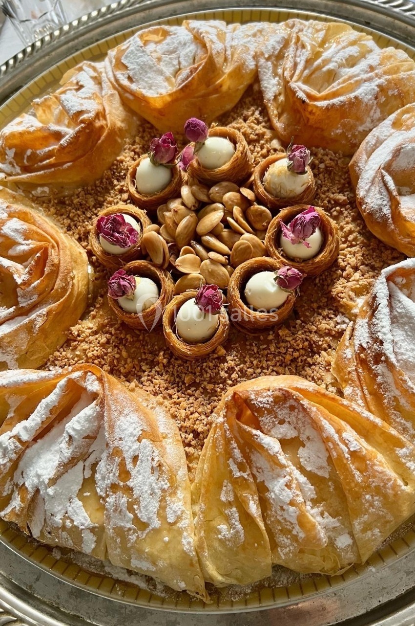 Assortiment de pâtisseries orientales en pâte fine, garnies d'amandes, de crème et décorées de fleurs séchées.