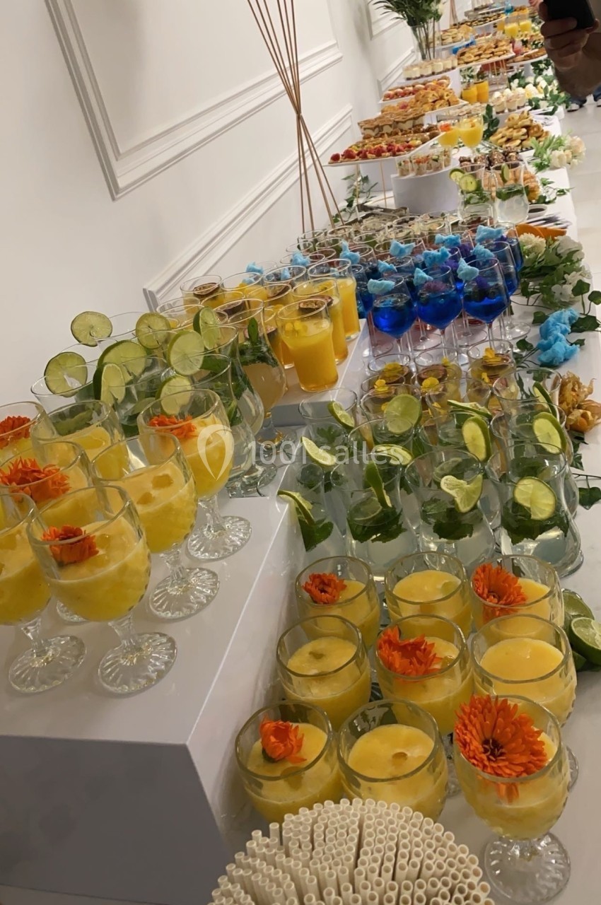 Buffet de boissons colorées disposées sur des tables, avec des verres garnis de fruits et de fleurs décoratives.