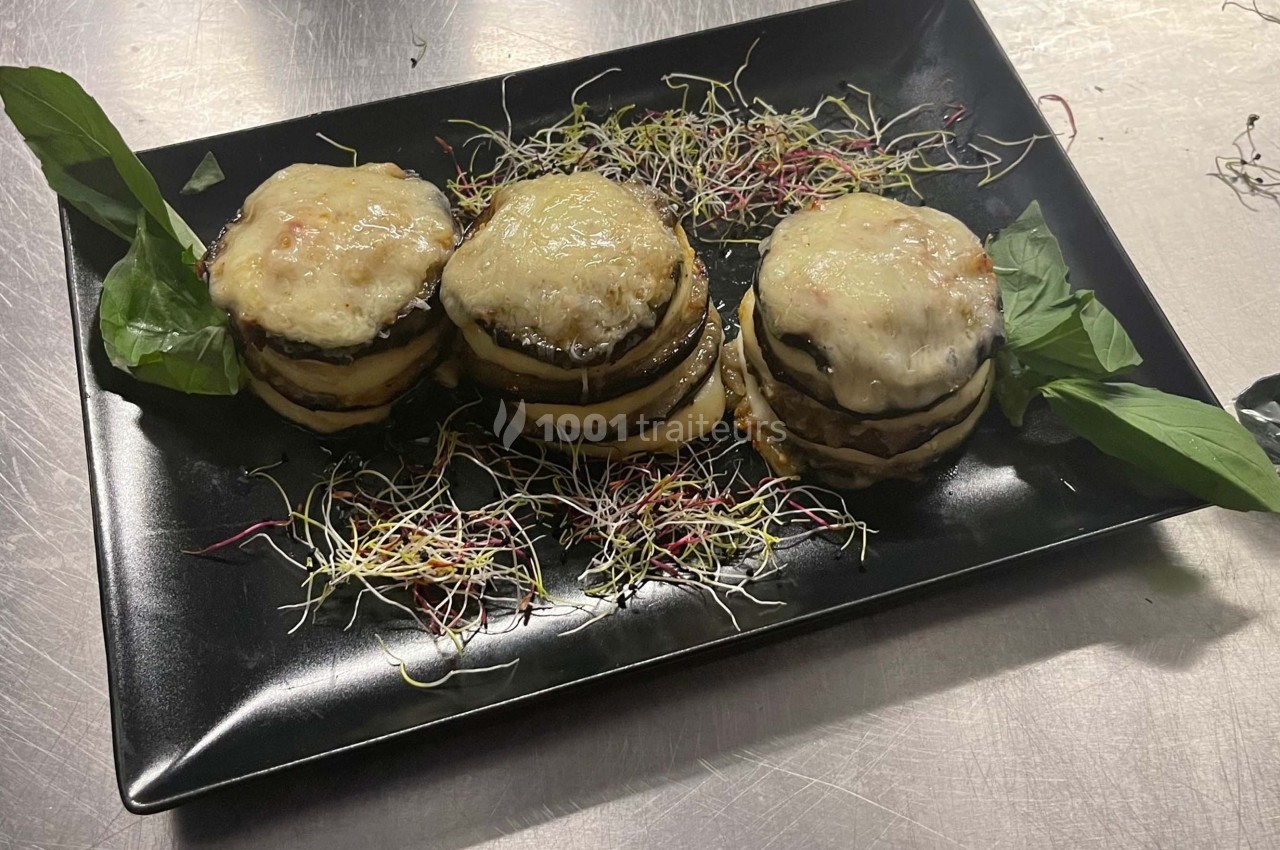 Assiette contenant trois millefeuilles d'aubergines gratinées, garnies de fromage fondu et entourées de pousses fraîches.