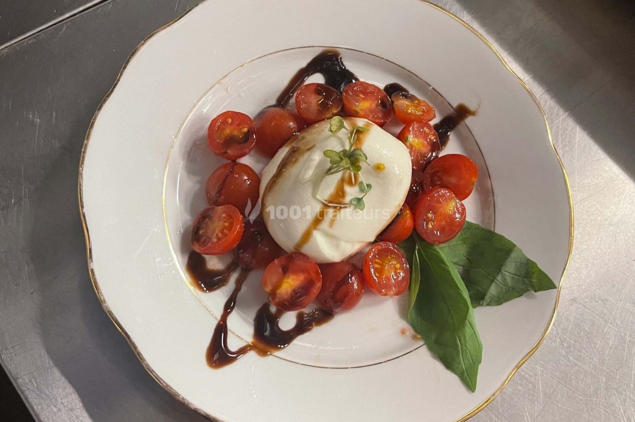 Assiette de burrata accompagnée de tomates cerises, basilic frais et filet de vinaigre balsamique.