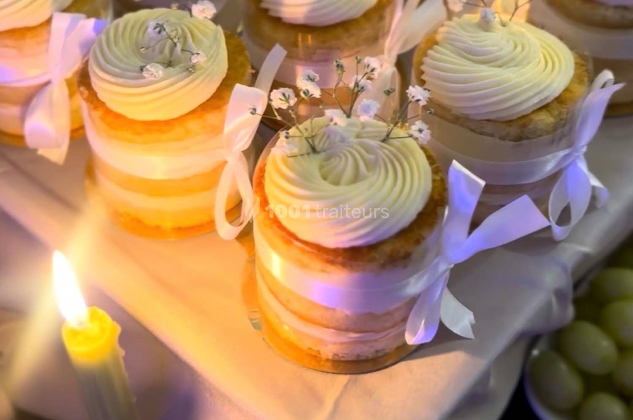 Petits gâteaux à étages décorés de crème et de fleurs blanches, entourés de rubans, éclairés par une bougie.