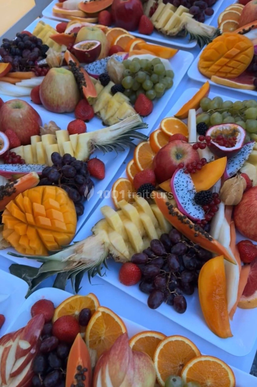 Assortiment de fruits frais variés disposés sur des plateaux, incluant mangues, raisins, pommes, oranges et fruits exotiques.