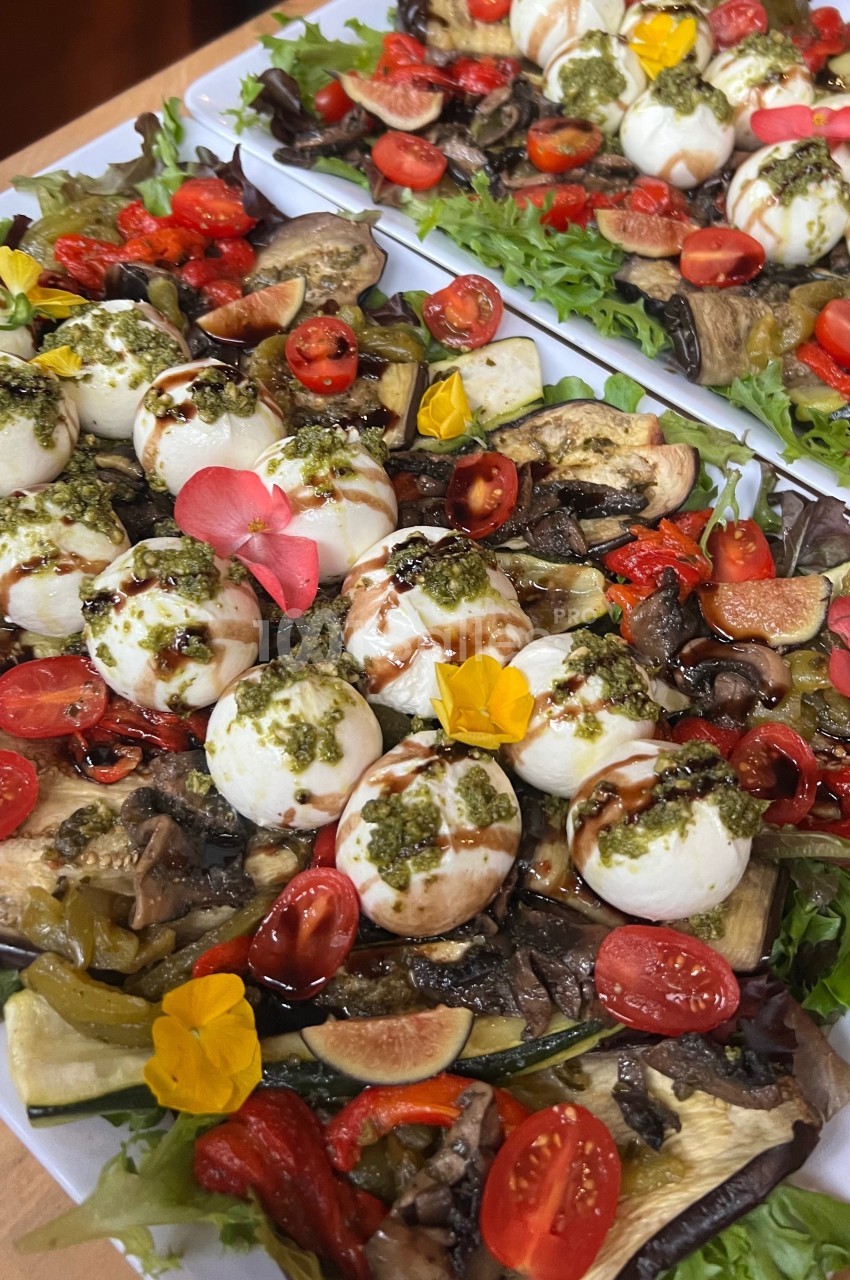 Plateaux de salade garnis de mozzarella, tomates cerises, légumes grillés, pesto, fleurs comestibles et vinaigre balsamique.