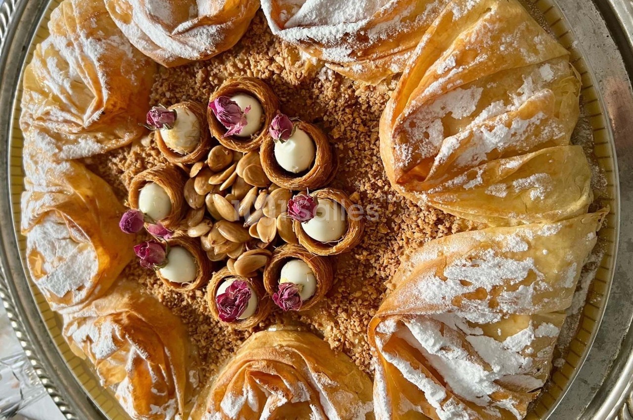 Plateau de pâtisseries orientales en pâte filo garnies d'amandes, de crème et décorées de fleurs séchées.