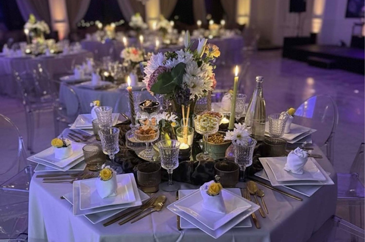 Table élégamment dressée avec vaisselle raffinée, bougies allumées et centre de table floral dans une salle de réception.