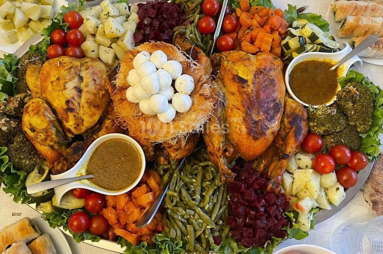 Plateau garni de poulets rôtis, légumes variés, sauces et garnitures, présenté sur un lit de feuilles de salade.