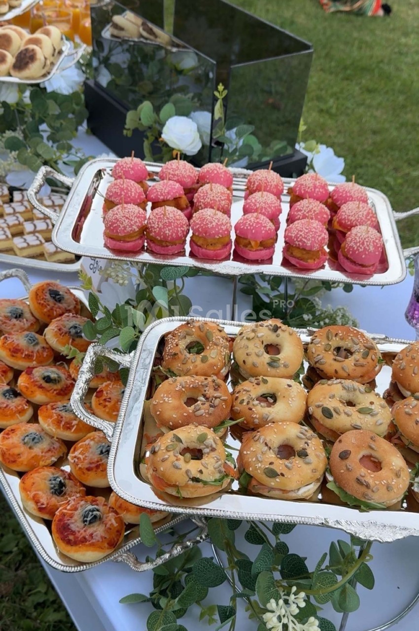 Plateaux de mini-pâtisseries et viennoiseries variées disposés sur une table décorée de feuillage, en extérieur.