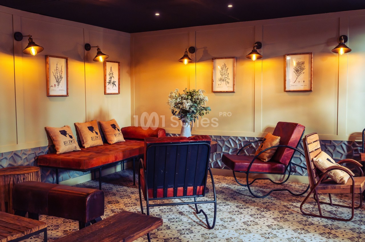 Salon chaleureux avec canapé en cuir, fauteuils vintage, décoration murale végétale et éclairage tamisé.