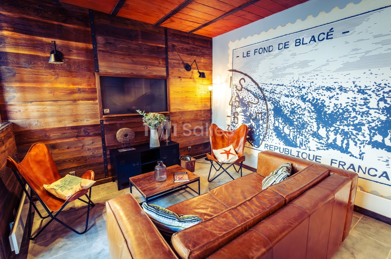 Salon chaleureux avec murs en bois, canapé en cuir, fauteuils design et grande affiche rétro en arrière-plan.