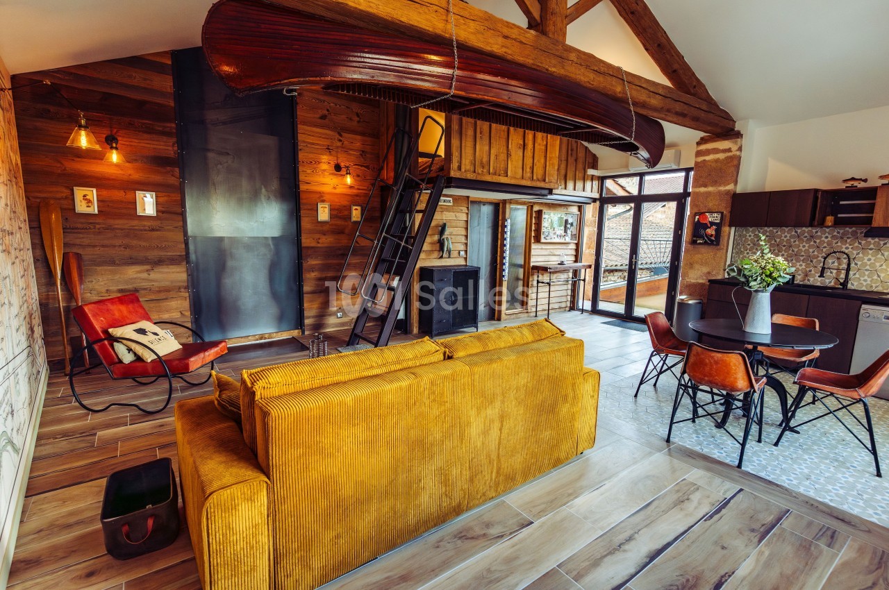 Salon chaleureux avec canapé jaune, mezzanine en bois, décoration rustique et cuisine ouverte dans un espace lumineux.