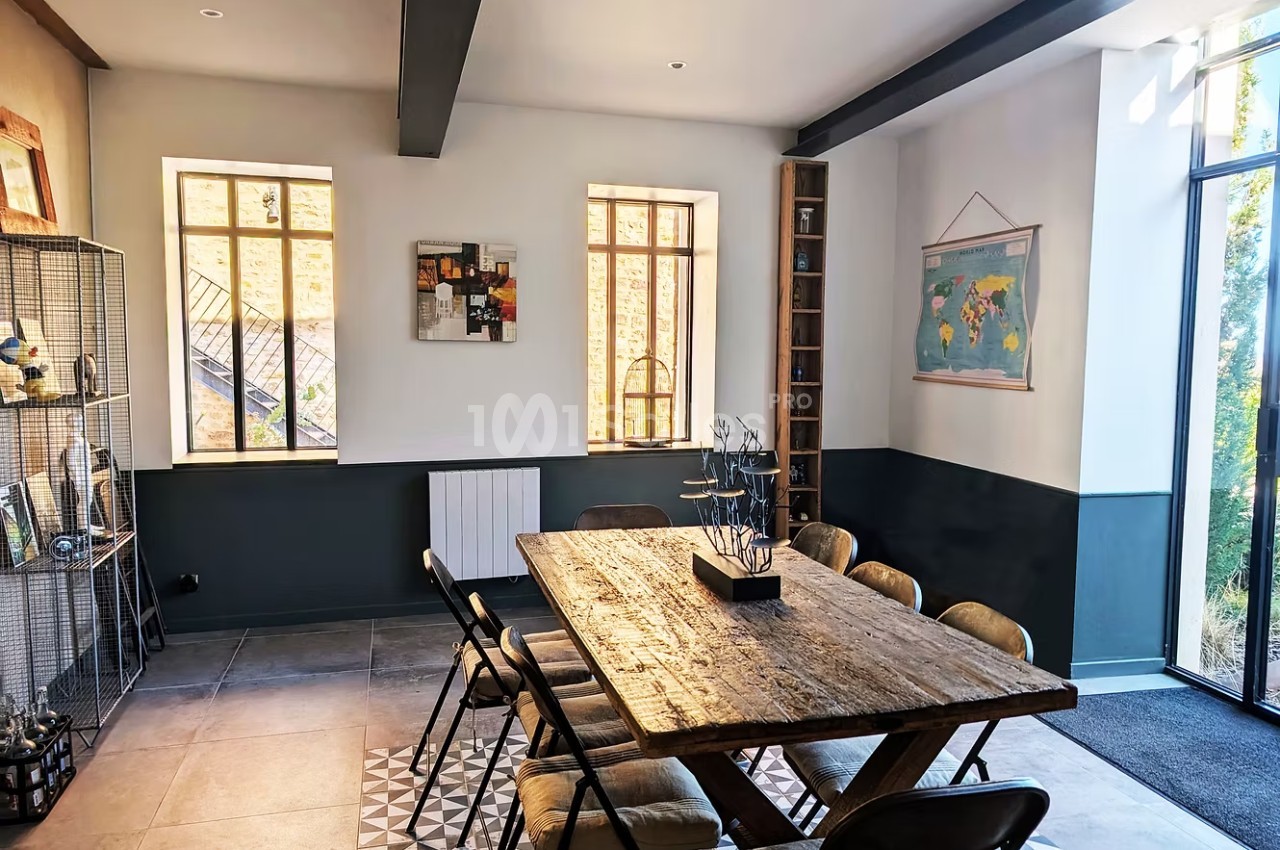 Salle à manger lumineuse avec une grande table en bois, des chaises métalliques et une décoration murale variée.