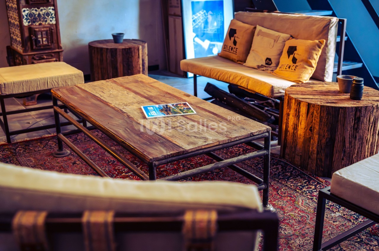 Salon avec table basse en bois, canapés et tabourets assortis, décoré d'un tapis et d'éléments rustiques.