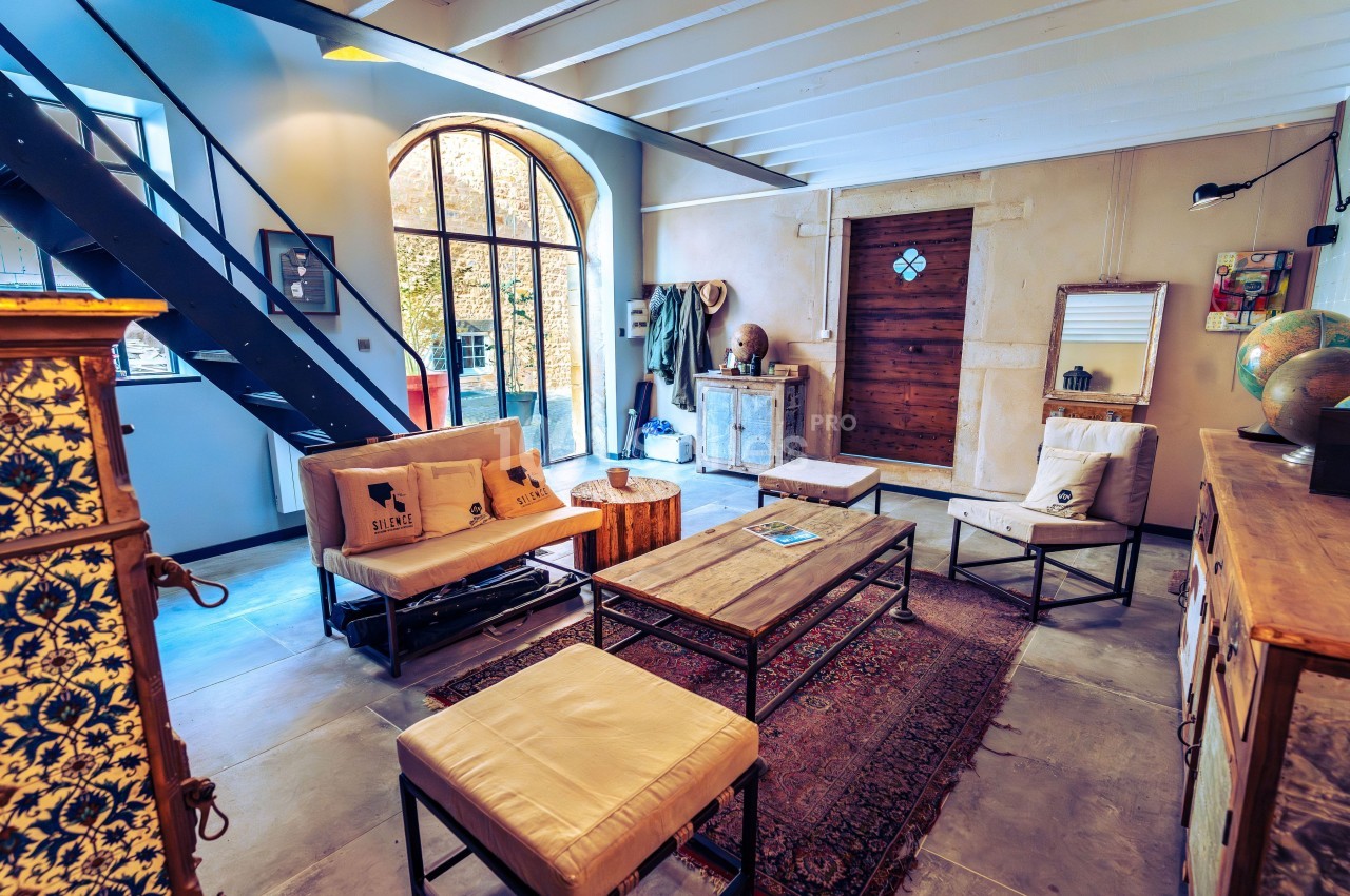 Salon lumineux avec mobilier en bois et métal, tapis au sol, grande baie vitrée et escalier en métal noir.