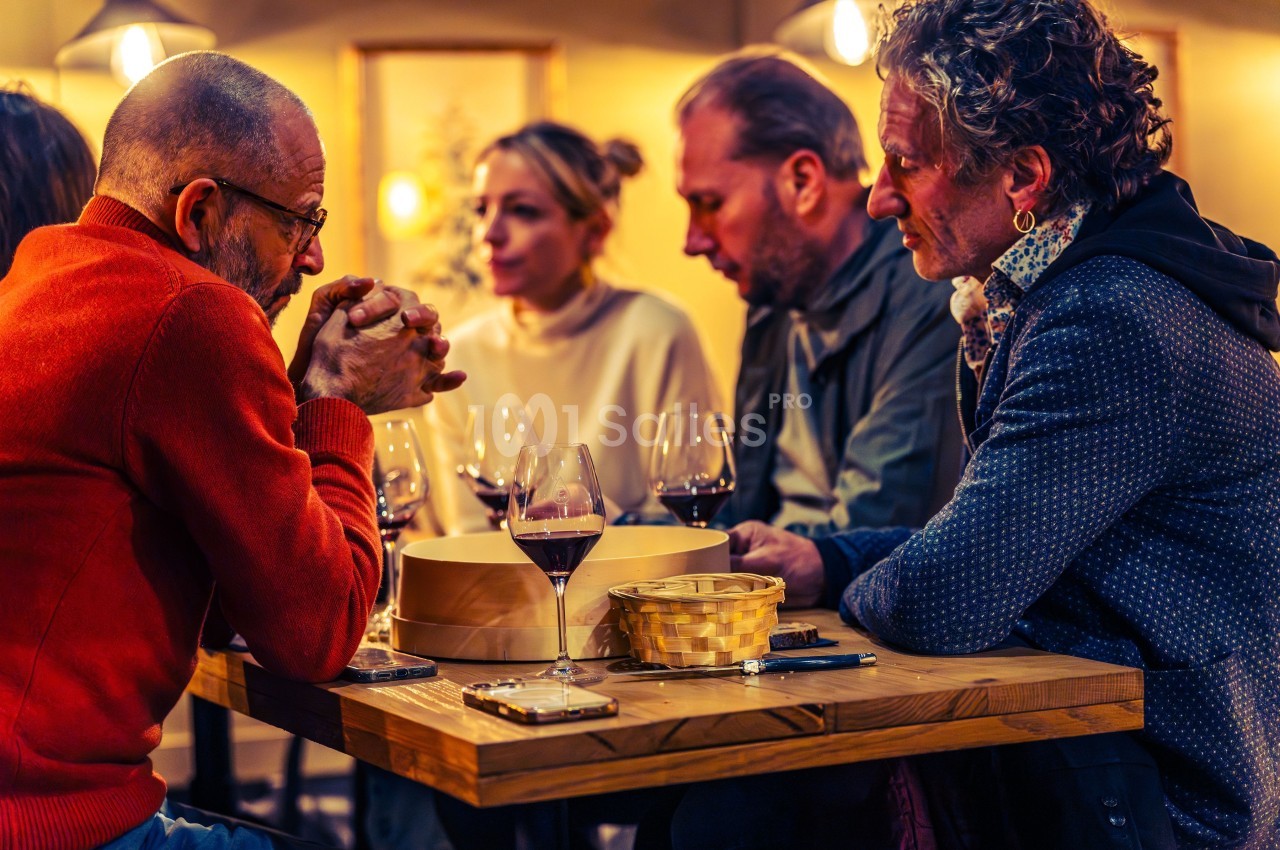 Quatre personnes discutent autour d'une table en bois avec des verres de vin et un panier au centre.