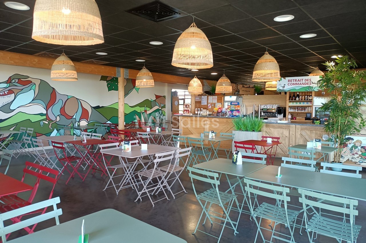 Salle de restaurant lumineuse avec tables et chaises colorées, décor mural végétal et comptoir de commande au fond.