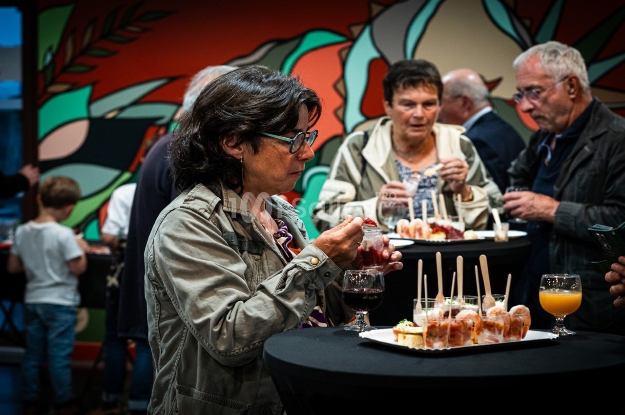 Des personnes debout autour de tables hautes dégustent des amuse-bouches lors d'un événement convivial.