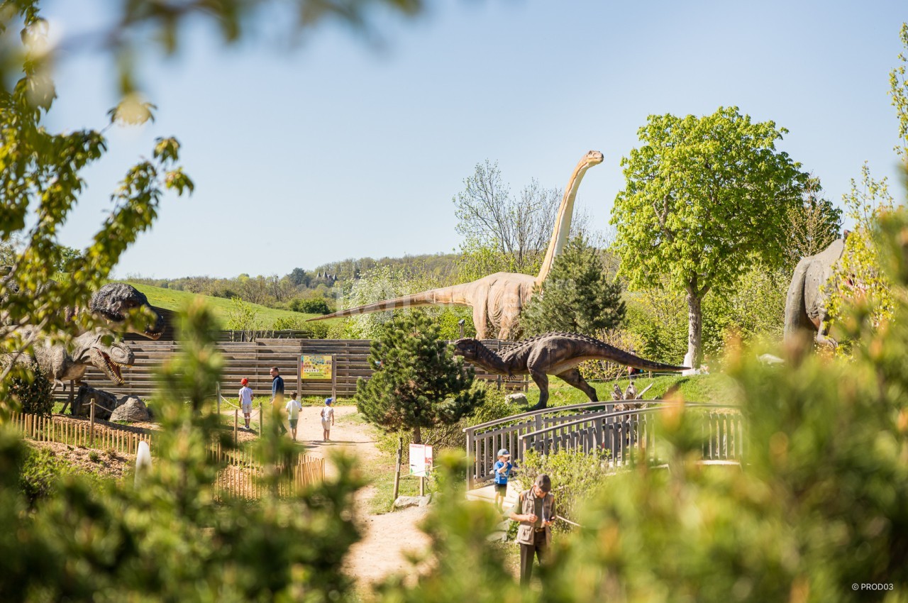 Des statues de dinosaures grandeur nature dans un parc verdoyant, avec des visiteurs en promenade.