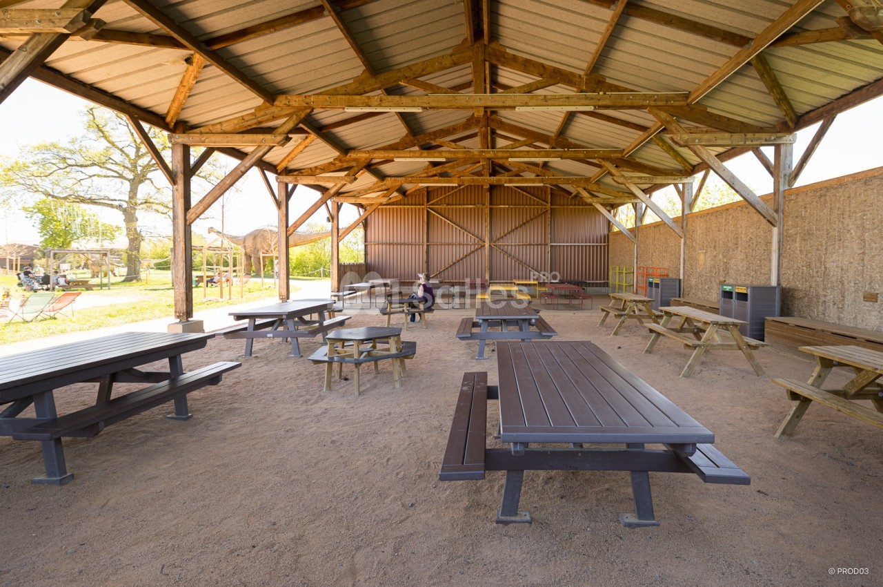 Abri en bois ouvert avec tables de pique-nique, situé dans un espace extérieur ensoleillé.