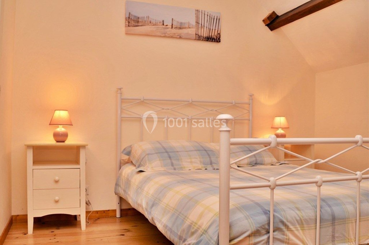 Chambre avec lit double en métal blanc, tables de chevet assorties et éclairage doux, décorée d'un tableau mural.