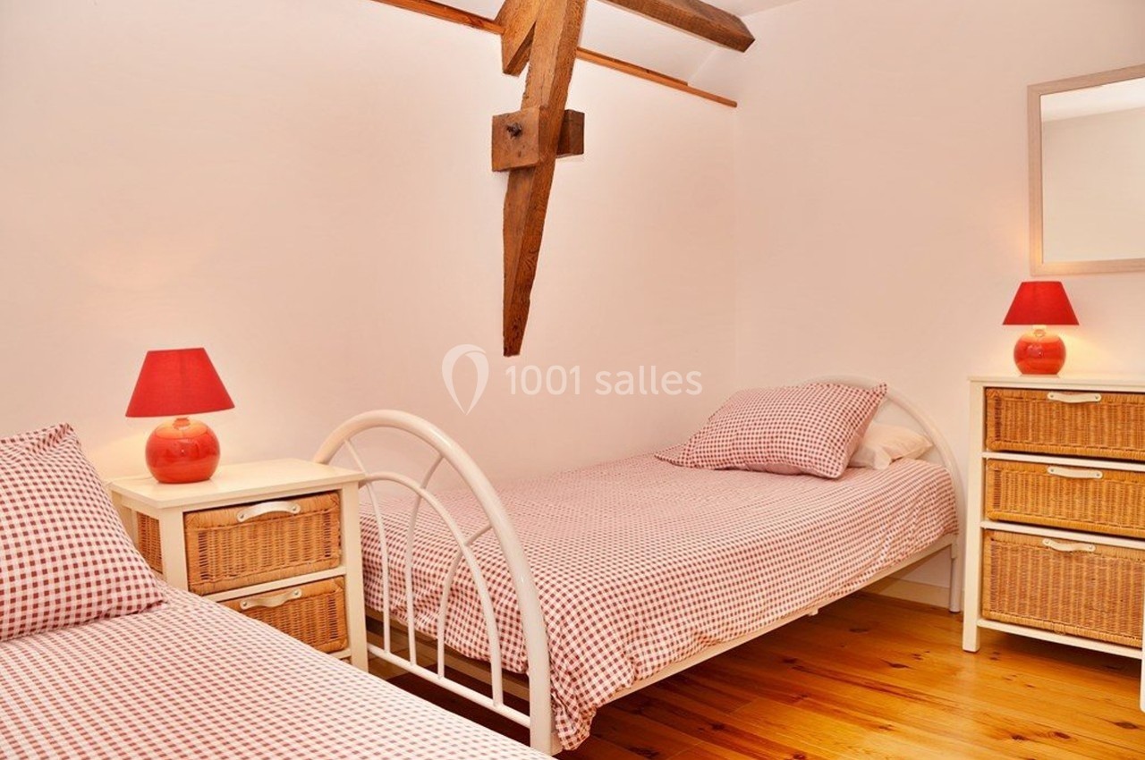 Deux lits simples avec linge à carreaux rouges, lampes assorties et meubles en osier dans une chambre lumineuse.