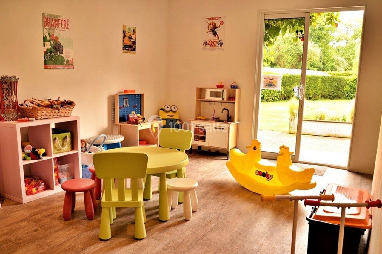 Salle de jeux lumineuse avec des meubles colorés, des jouets variés et une porte-fenêtre donnant sur un jardin.