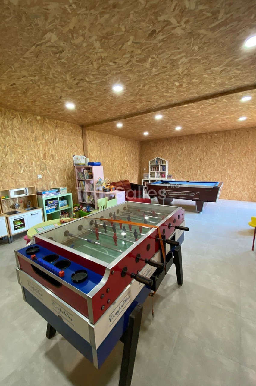 Salle de jeux avec baby-foot, billard, jouets pour enfants et mobilier coloré, dans un espace aux murs en bois.