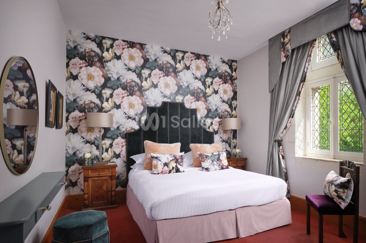 Chambre élégante avec un lit double, papier peint floral, fenêtres à vitraux et mobilier classique en bois.
