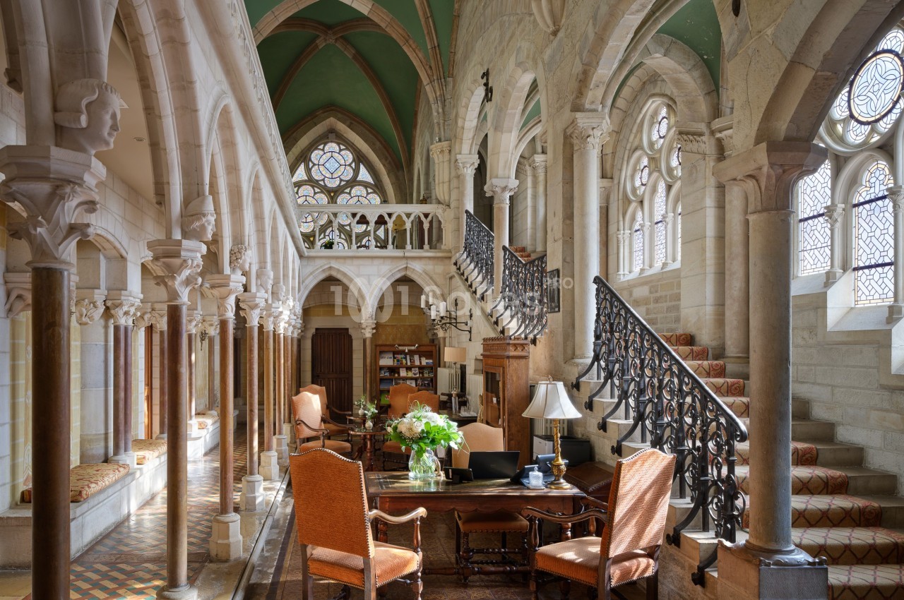 Intérieur lumineux d'un bâtiment historique avec colonnes, arches, escalier en fer forgé et mobilier classique.