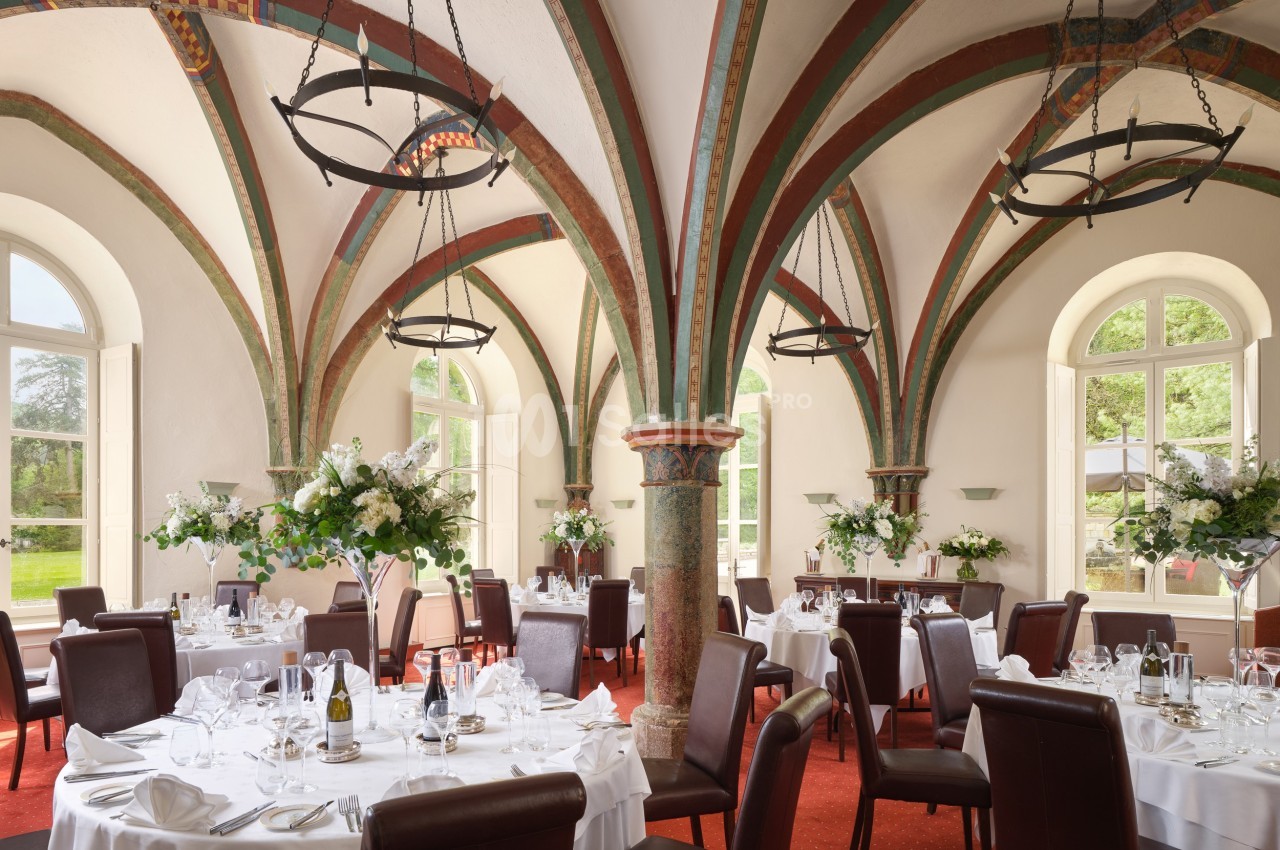 Salle de réception élégante avec tables dressées, arches colorées et grandes fenêtres laissant entrer la lumière naturelle.